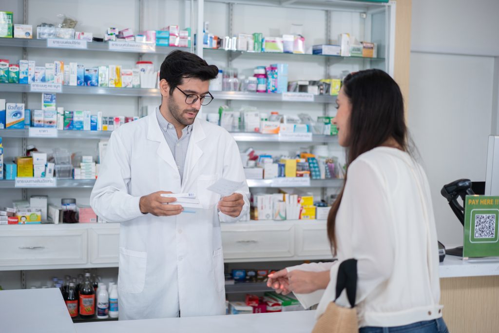 Kobieta w aptece, konsultująca receptę z farmaceutą.